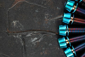 A row of blue Titanium bicycle screws on a black textured background with free space