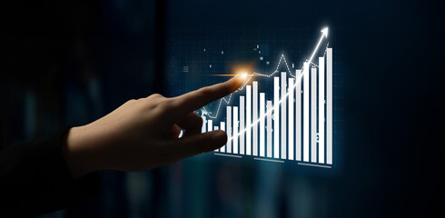 A hand gestures toward a digital display with an upward-trending graph and bar chart, symbolizing business growth, data analysis, and technological advancement. Impute