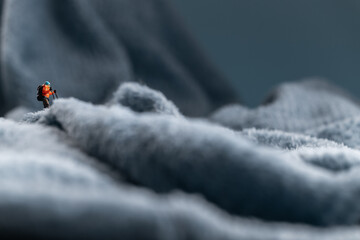 A miniature mountain climber figurine on a fuzzy fleece lining resembling a snow-covered surface, with a blurred background of a mountain or ice wall