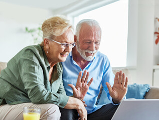 Portrait of a lovely senior mature couple using a laptop together and having video call sitting on sofa at home