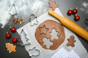Top view of gingerbread cookie preparation with star, tree, and gingerbread man cutters beside a rolling pin and holiday ornaments. Great for Christmas promotions, seasonal digital content.