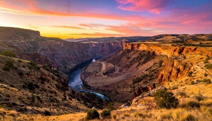 Vast canyon landscape at sunset with a winding river below and dramatic pink and orange sky above in golden hour lighting