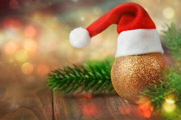 golden Christmas ball in a Santa Claus hat peeks out from behind the branches of the Christmas tree in sparkling lights of garlands