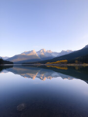 Obraz premium Lake with mirrorlike reflection of distant peaks, vibrant trees, morning light, wideangle, pristine mountain escape