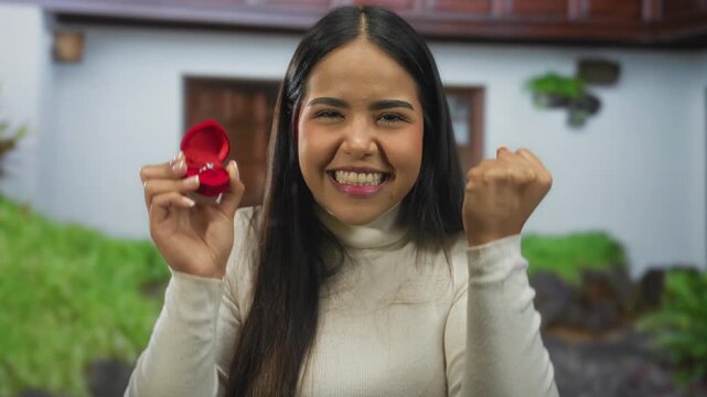 Young woman celebrating engagement holding ring outdoors, smiling with joy.