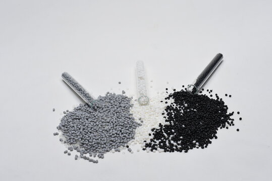 Granules of gray, black and white plastic fall out of the test tube in a heap on white background