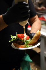 chef de hamburguesa echando salsa de mahonesa a una hamburguesa de carne y vegetales