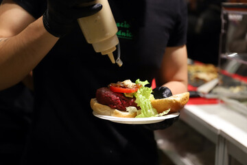 chef preparando una hamburguesa de carne y echándole salsa de mahonesa