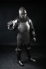 Obraz premium Portrait of a medieval knight in a closed helmet and a full set of armor with a sword in his hand isolated on a dark background