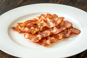 Naklejka premium Crispy fried bacon slices neatly arranged on simple white serving plate