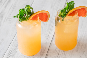 Two chilled Paloma cocktails with grapefruit slices and mint sprigs on white wood