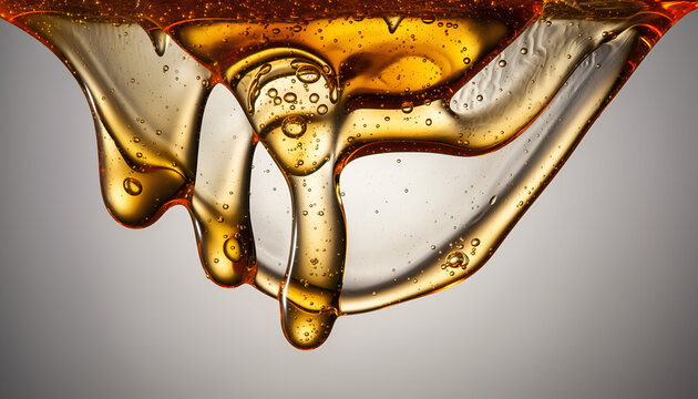 Viscous golden liquid honey dripping in abstract macro close up with air bubbles and light reflections on a neutral gray background with studio lighting