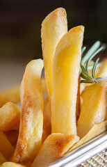 Golden french fries in metal basket with rosemary on wood
