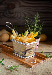 Golden french fries in metal basket with rosemary on wood