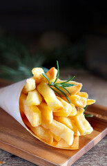 Golden french fries in metal basket with rosemary on wood