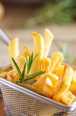 Golden french fries in metal basket with rosemary on wood
