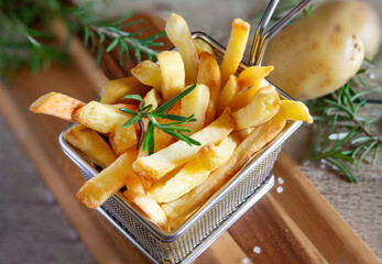Golden french fries in metal basket with rosemary on wood