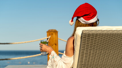 Woman in Santa's hat by the sea in a sun lounger
