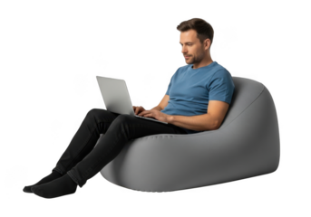 A focused man in casual attire sits comfortably on a large beanbag chair actively typing on his laptop computer isolated on transparent background