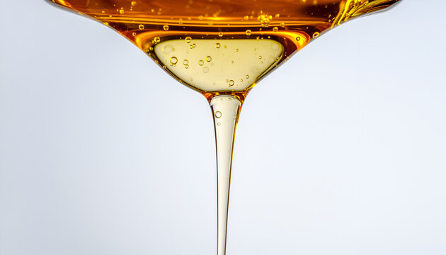 Viscous Golden Amber Liquid Dripping Slowly Forming a Thin Stream with Tiny Bubbles Suspended Throughout Against a Soft Light Grey Background