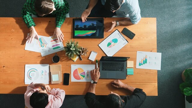 Top view of diverse businesspeople discuss about financial plan at meeting while looking at stock market statistic and explain marketing idea at meeting room. Creative startup concept. Convocation.
