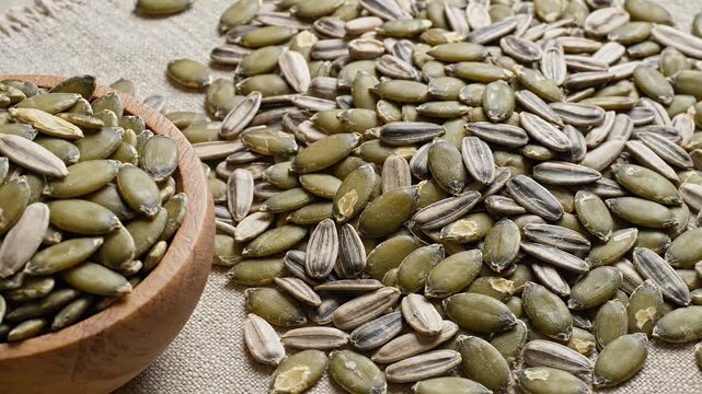 Close up of healthy pumpkin and sunflower seeds mix a nutritious snack for a balanced diet scattered on a rustic fabric background and in a wooden bowl