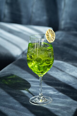 Cocktail on blue background. Melon spritz drink placed on the couch at the bar, night club or restaurant. Glass of refreshing alcoholic beverage. Stylish, modern summer terrace menu. Vertical