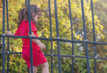A girl in a red costume climbs a rope net against the backdrop of green trees