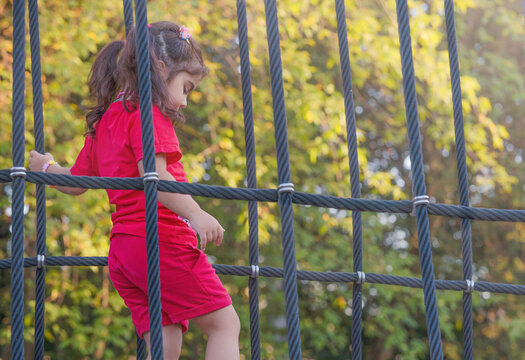 A girl in a red costume climbs a rope net against the backdrop of green trees
