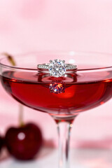 Engagement ring resting on a vibrant cherry cocktail with a soft pink background