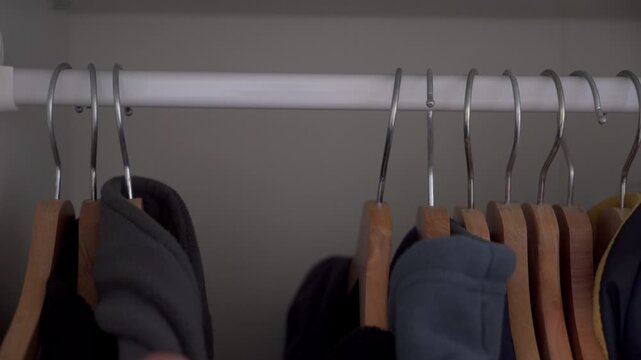 A close-up of a closet interior shows wooden hangers with metal hooks being pushed or pulled along a white rod. The movement creates a distinct metallic clatter and scrape sound.