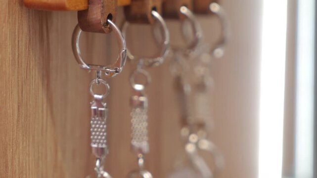A close-up of several silver metal keychains hanging from a wooden key rack shows them being moved. The movement causes the chains and rings to strike each other