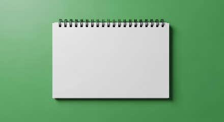 A blank spiral notebook resting on a green surface in a horizontal orientation with a simple composition