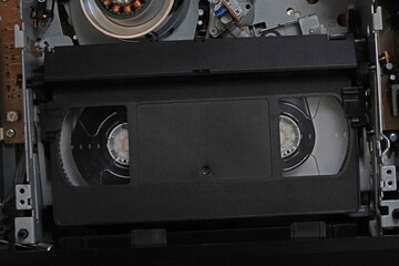 An unlabeled, vintage VHS tape is shown in a VCR machine unit up close.