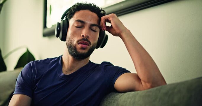 Sad, headphones and man on sofa in home listening to music with depression, thinking or mental health. Upset, audio tech and person with playlist or radio for emotions in living room at apartment.