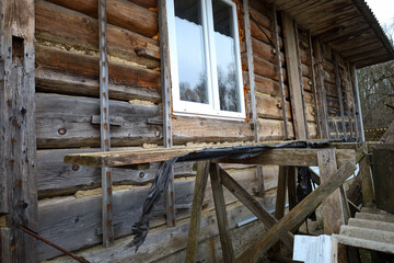 This shot features the exterior wall of an old wooden log house undergoing renovation, showcasing horizontal logs and a new white plastic window.