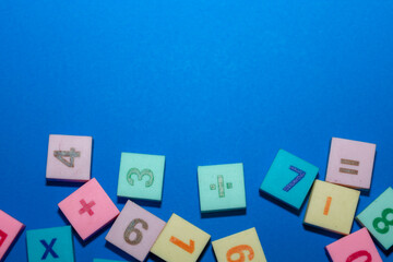 This close-up shot features a cluster of multi-colored square tiles with embossed numbers and mathematical symbols set against a saturated blue background.