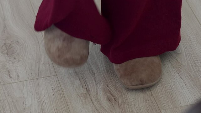 Fuzzy slippers and pant legs on a laminate floor. A person stamps their foot on the floor. A sudden, blunt thud and bump sound results from the action.
