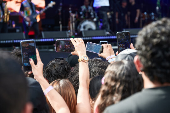 
Close-up of concert audience hands holding multiple smartphones to record the dimly lit band performing on stage. The image highlights the modern trend of capturing and sharing live music experiences - Powered by Adobe