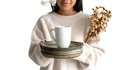 Person holding stack of plates with a mug and dried flowers, sweater, smiling