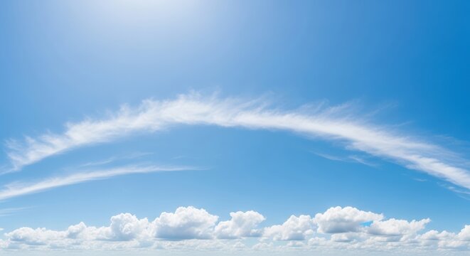 Expansive panoramic view of a clear blue sky with wispy cirrus clouds forming an arc and cumulus clouds scattered near the horizon under bright sunlight