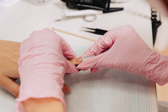Close-up of a manicurist in pink gloves carefully placing a nail extension form template onto a client's finger for gel or acrylic nail modeling.