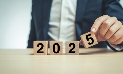 Naklejka premium Businessman adding a wooden block to spell 2025 representing the new year and future planning on a bright surface