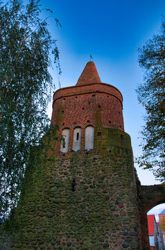 Fototapeta Strzelce Krajeńskie – Wieża Więzienna – Zabytkowa wieża z czerwonej cegły z kamiennym murem o zmierzchu pod błękitnym niebem.