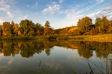 A riverside landscape on a sunny autumn morning. The calm surface of the water. An autumn morning on the banks of a narrow rural river.