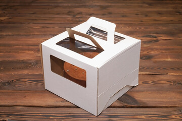  Delicious chocolate cake in a white folding cardboard box on wooden boards.