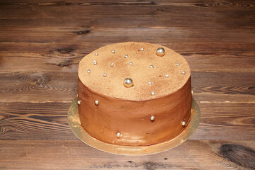 Baked goods. Chocolate cake with dragees on a golden base, on a wooden table.