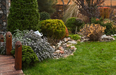 Obraz premium Beautiful garden with a variety of plants and green lawn, neatly arranged along a stone path. Lush green garden with colorful plants and trees, featuring a well-maintained lawn.