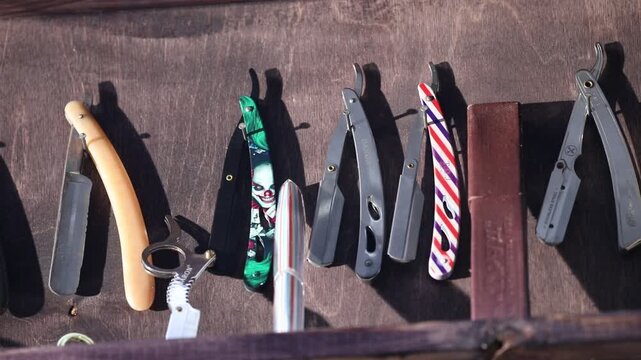 Collection of professional straight razors displayed on a dark wooden wall, featuring vintage designs, colorful plastic. Essential tools for a traditional barbershop shave and expert male grooming.