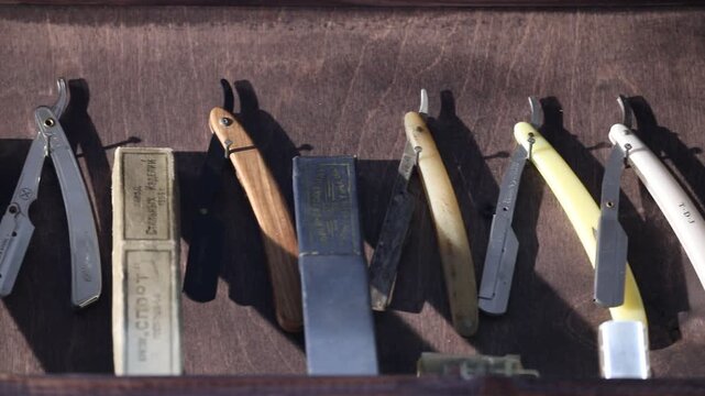 Collection of professional straight razors displayed on a dark wooden wall, featuring vintage designs, colorful plastic. Essential tools for a traditional barbershop shave and expert male grooming.